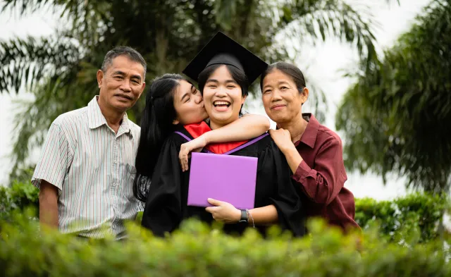 College graduate smiling and holding diploma while celebrating with family