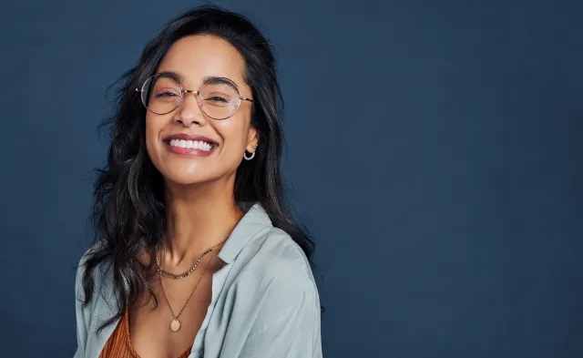 Beautiful university student having fun isolated against blue wall while wearing specs.