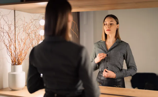 Self-confident woman looking at her reflection into the mirror indoors.