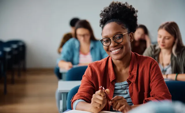 Happy African American woman attending a lecture in university classroom and looking at camera.