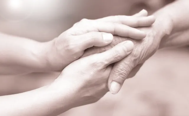 Caregiver, career hand holding elder hand in hospice care. 