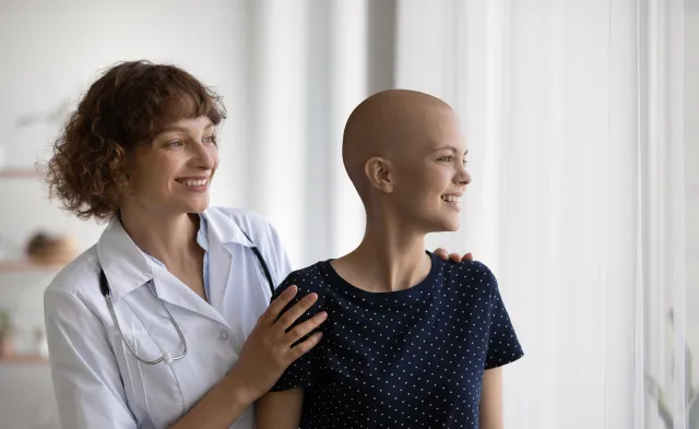 Smiling Caucasian doctor or nurse support comfort millennial woman struggle with oncology. Happy GP and optimistic female cancer patient look in distance dream of illness recovery or remission.