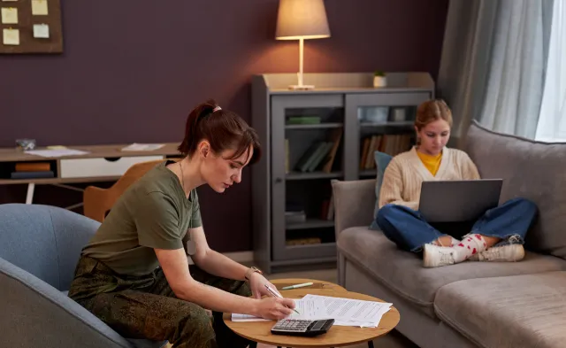 Side view portrait of young military woman working with documents at home, daughter in background, copy space