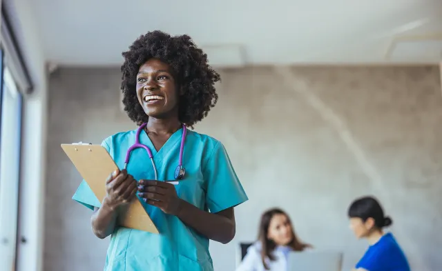 Practical nurse in teal scrubs wearing stethoscope and holding clipboard in medical office