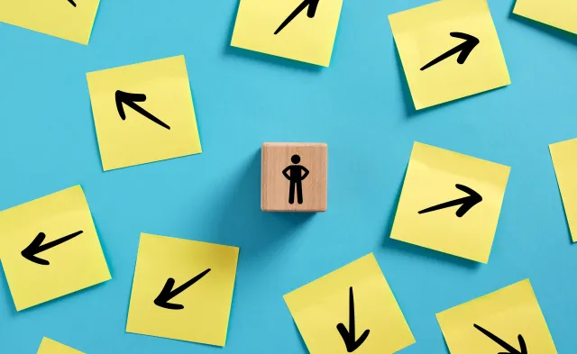 Decision making in business. Choosing a path to follow. Businessman standing on a wooden block, surrounded by arrows pointing in various directions.