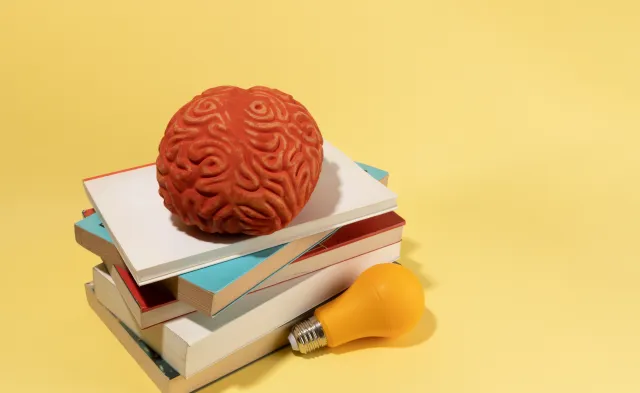 A brain, a bulb and books on yellow background, creative concept, ideas.