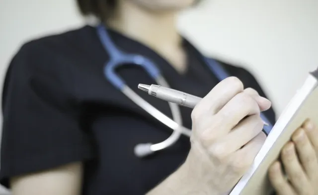 Health professional wearing stethoscope writing on pad of paper