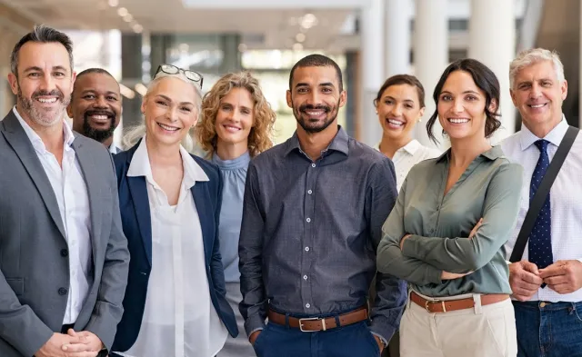 A diverse group of eight smiling business professionals standing together in a bright, modern office.