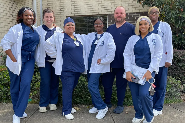 Group of Herzing online MSN Direct Entry students in white coats posing for photo smiling outdoors