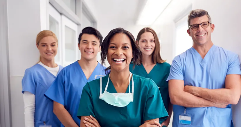 Smiling healthcare professionals in scrubs stand together in a bright, modern medical setting, symbolizing teamwork and dedication in healthcare.