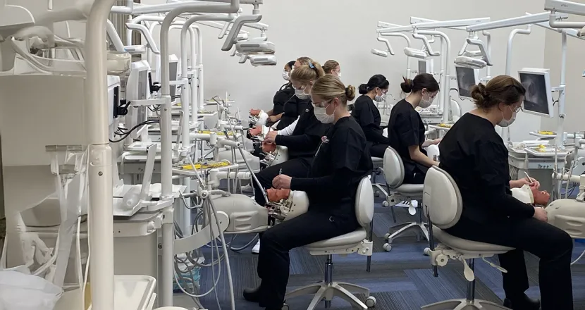Herzing University dental hygiene students practicing in a state-of-the-art lab, each seated at individual workstations with dental equipment and training mannequins.