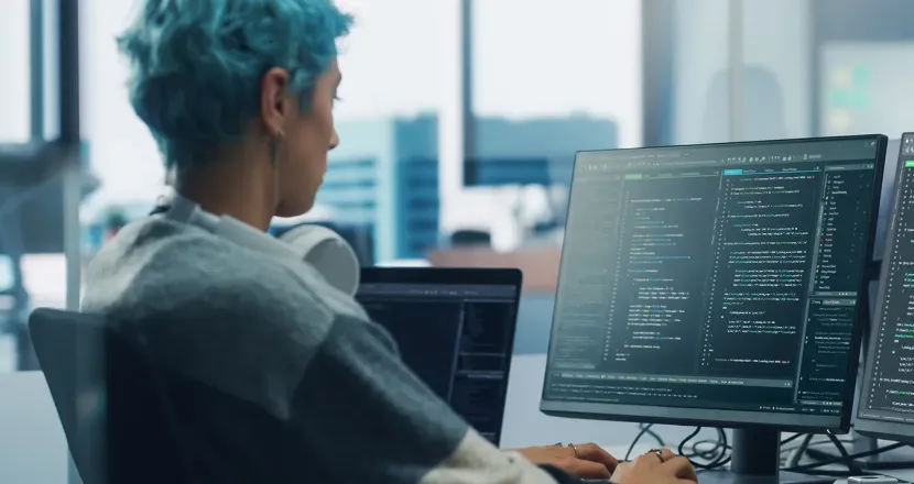 Application programmer seated in front of dual monitors in office environment coding