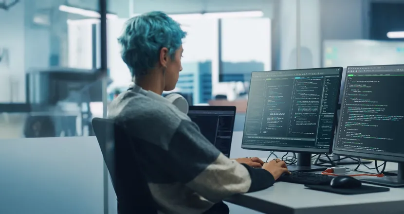 Application programmer seated in front of dual monitors in office environment coding