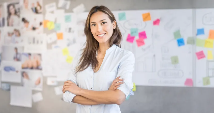 Smiling marketing professional standing in front of creative project board with colorful sticky notes