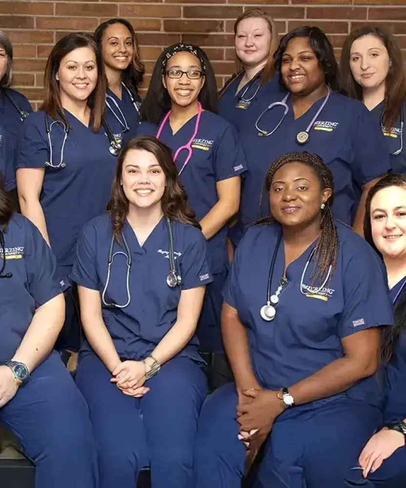 Group of LPN to RN students wearing blue scrubs smiling for picture in front of brick wall