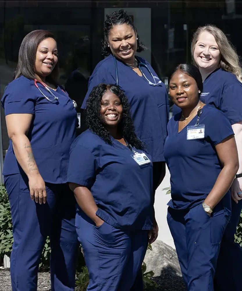 ASN students from Herzing University stand together outside a campus building wearing navy blue nursing scrubs.