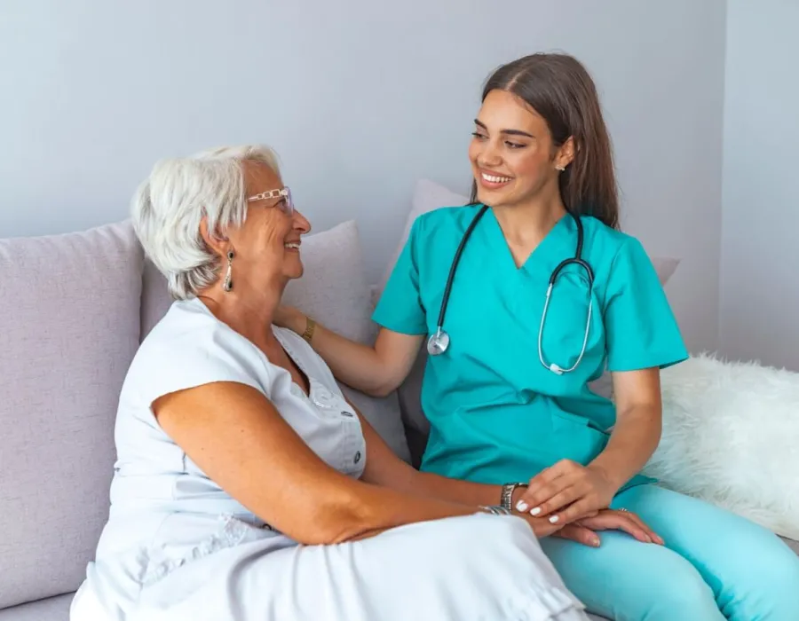 Home health nurse speaking with elderly client on couch in home