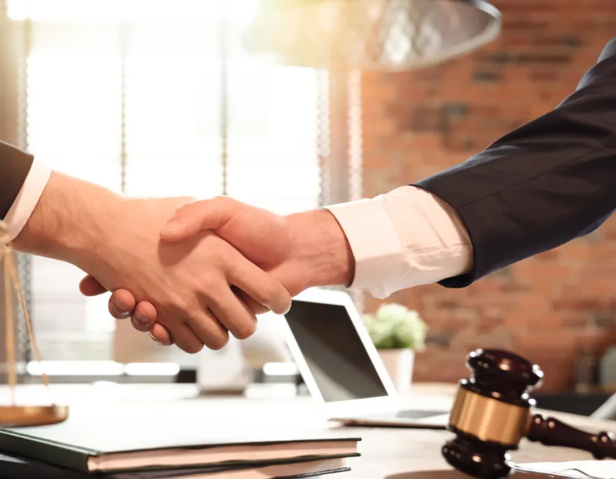 Two lawyers shaking hand across desk with gavel rested on it