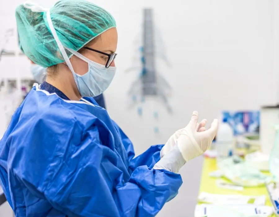 Sterile processing tech wearing mask and additional PPE cleaning surgical instrument in clean room