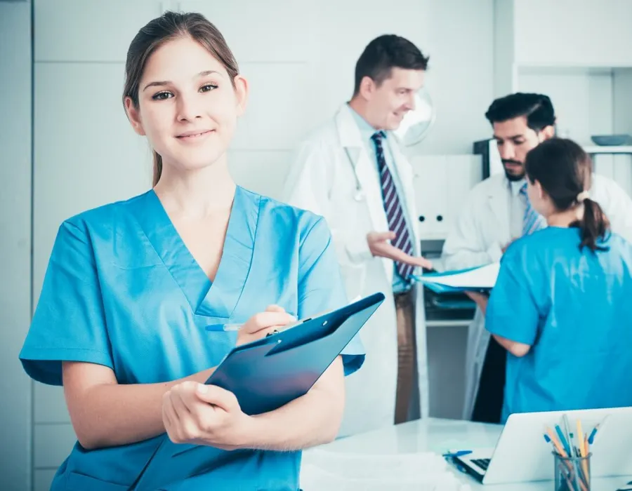 Medical assistant in hospital room with patient holding clipboard and smiling