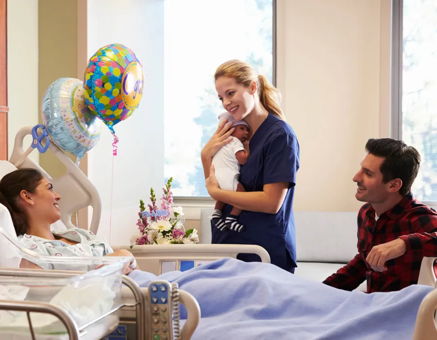 Labor and Delivery Nurse Holding Infant and Smiling with New Parents