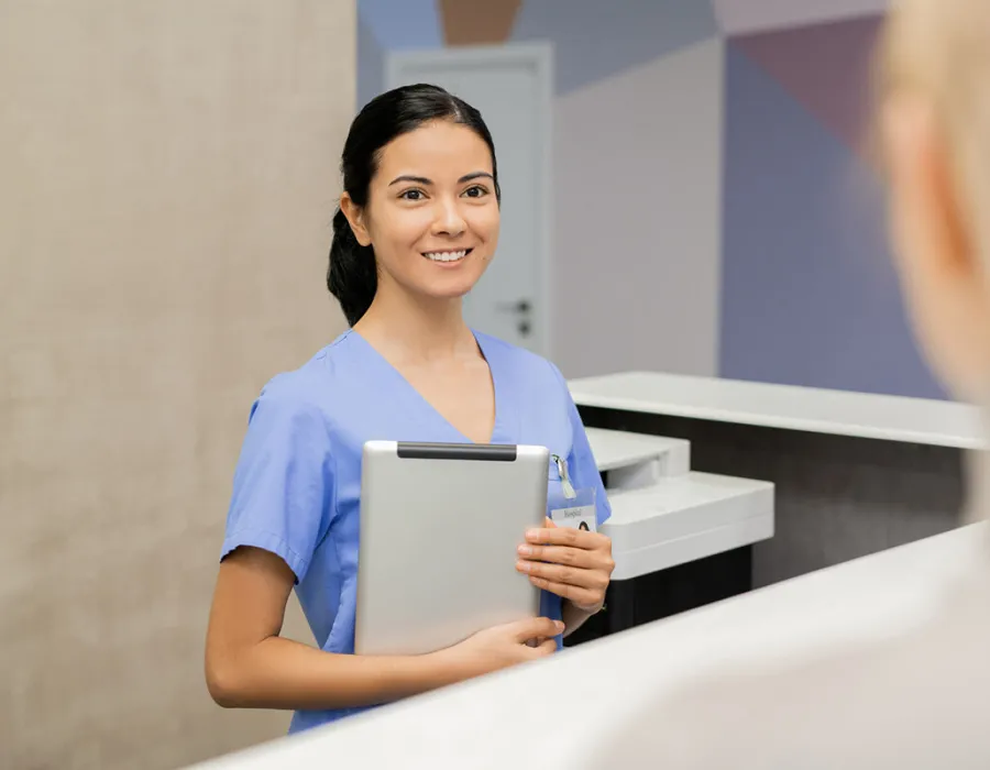 Medical assistant at front desk holding tablet smiling with patient