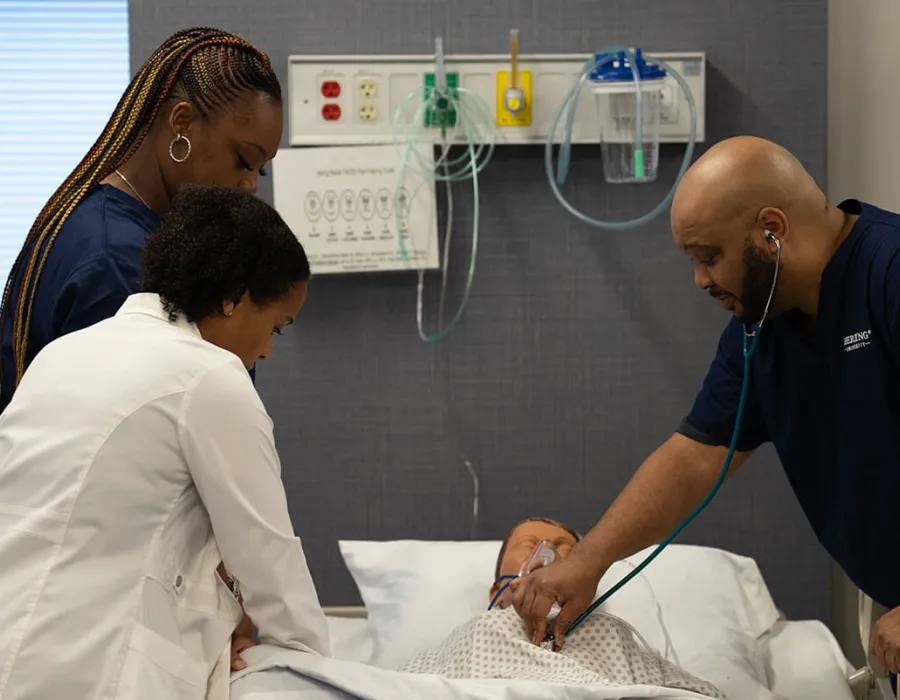 Herzing nursing students practicing reading heart rate with nursing instructor during simulation lab