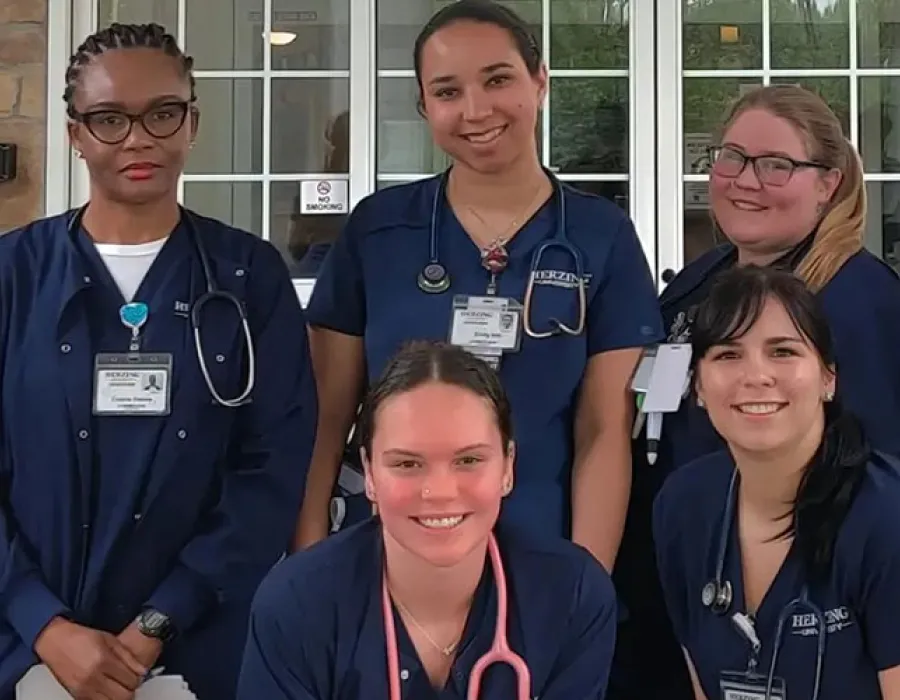 Group of Herzing nursing students in blue scrubs smiling for photo