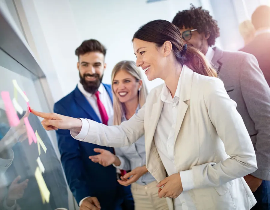 Project manager leading team meeting pointing to post it notes on glass project board