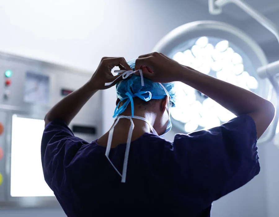 Surgical technologist fastening mask in preparation before surgery in operating room