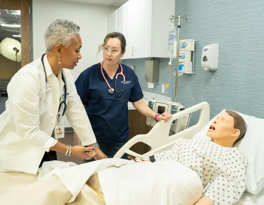 Nurse educator instructing practical nurse in simulation lab about basic patient care