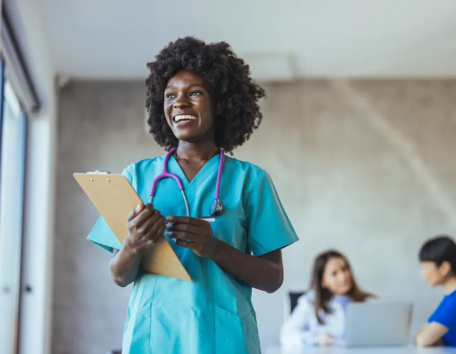 Practical nurse in teal scrubs wearing stethoscope and holding clipboard in medical office