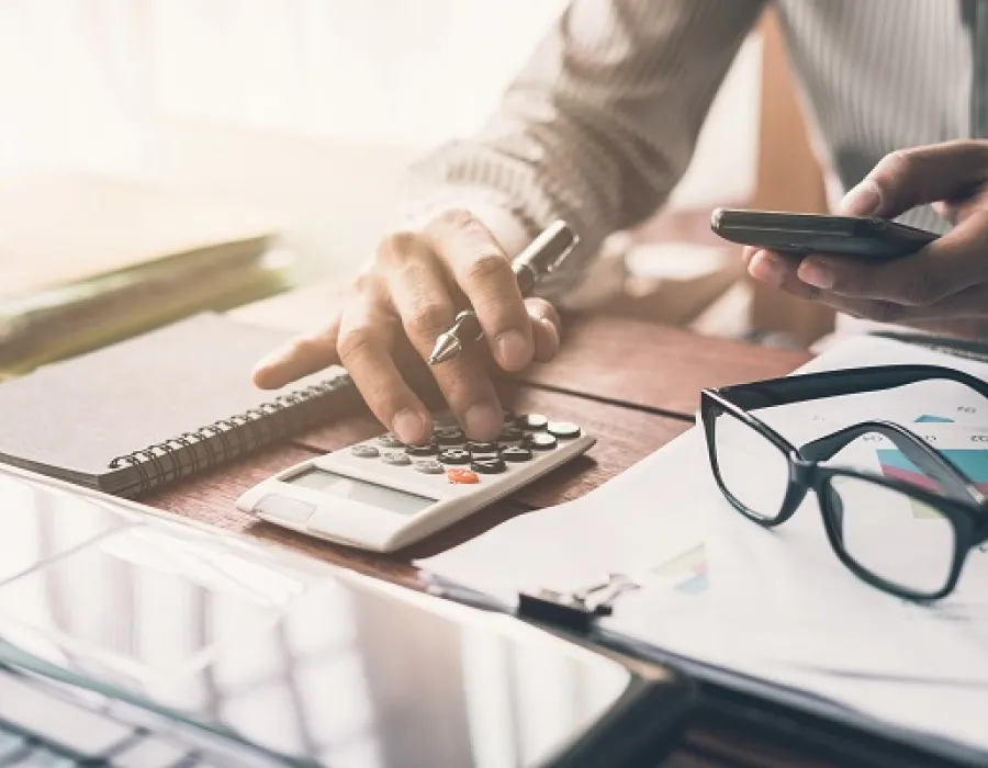 Accountant seated at desk punching numbers into calculator while comparing with notes