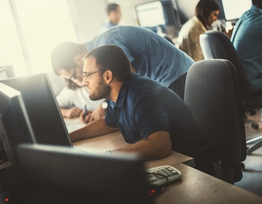 Computer programmer seated at desk in busy office writing code for project