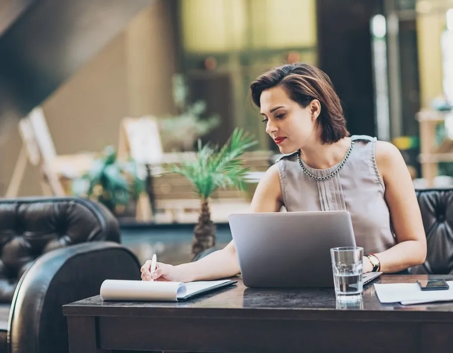 Paralegal seated in lobby in front of laptop while taking notes on notepad