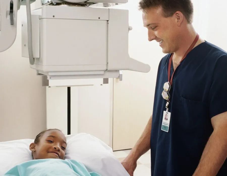 Pediatric nurse speaking with young patient and smiling at bedside in hospital room