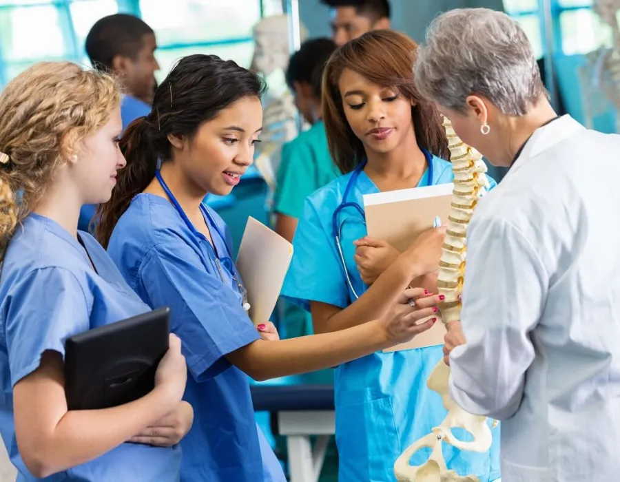 Three nursing students learning skeletal structure from nurse teacher