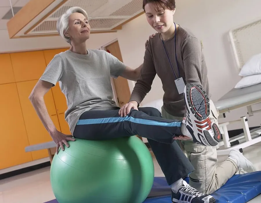 Physical therapist assistant providing PTA services for patient stretching on exercise ball