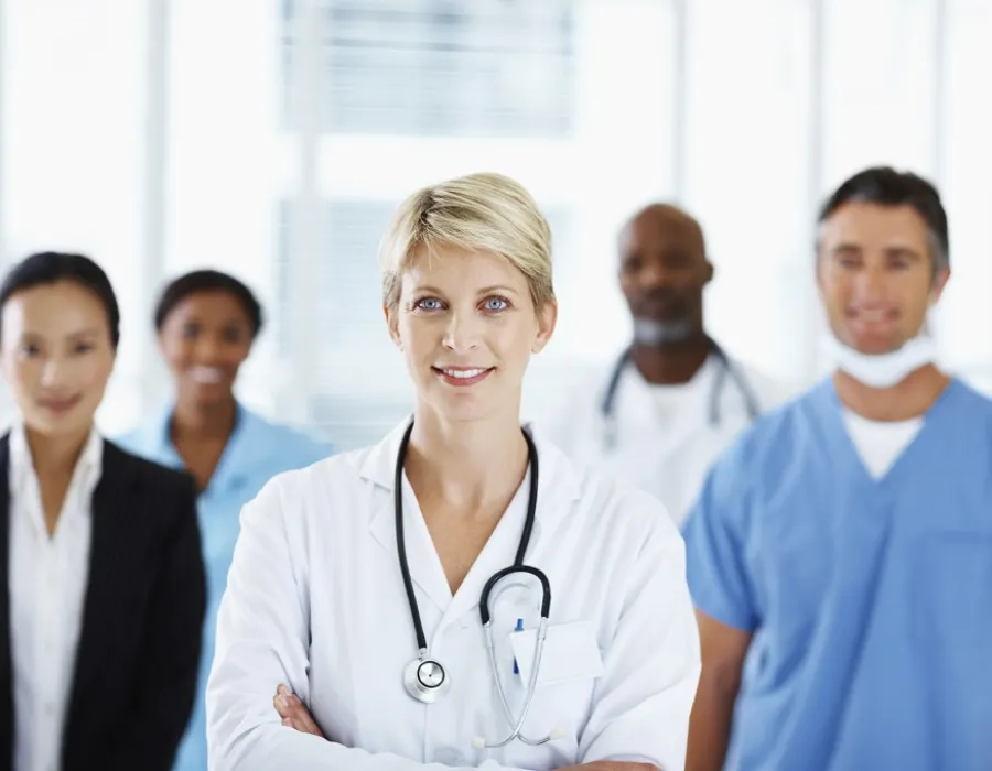 Healthcare manager in white coat smiling in front of group of healthcare staff and administrators