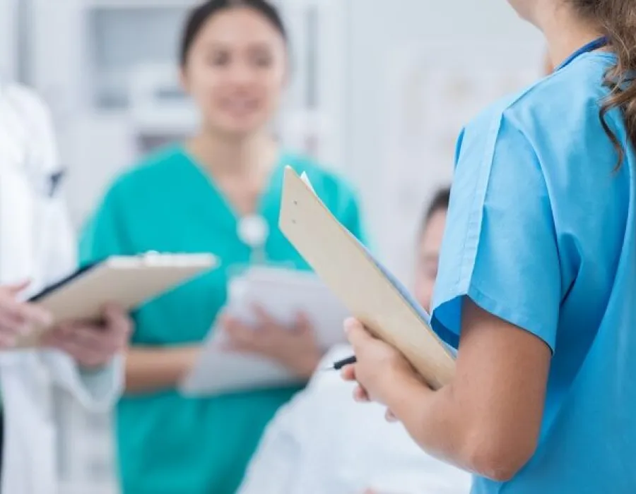 Registered nurse holding clipboard speaking with nursing staff including family nurse practitioner