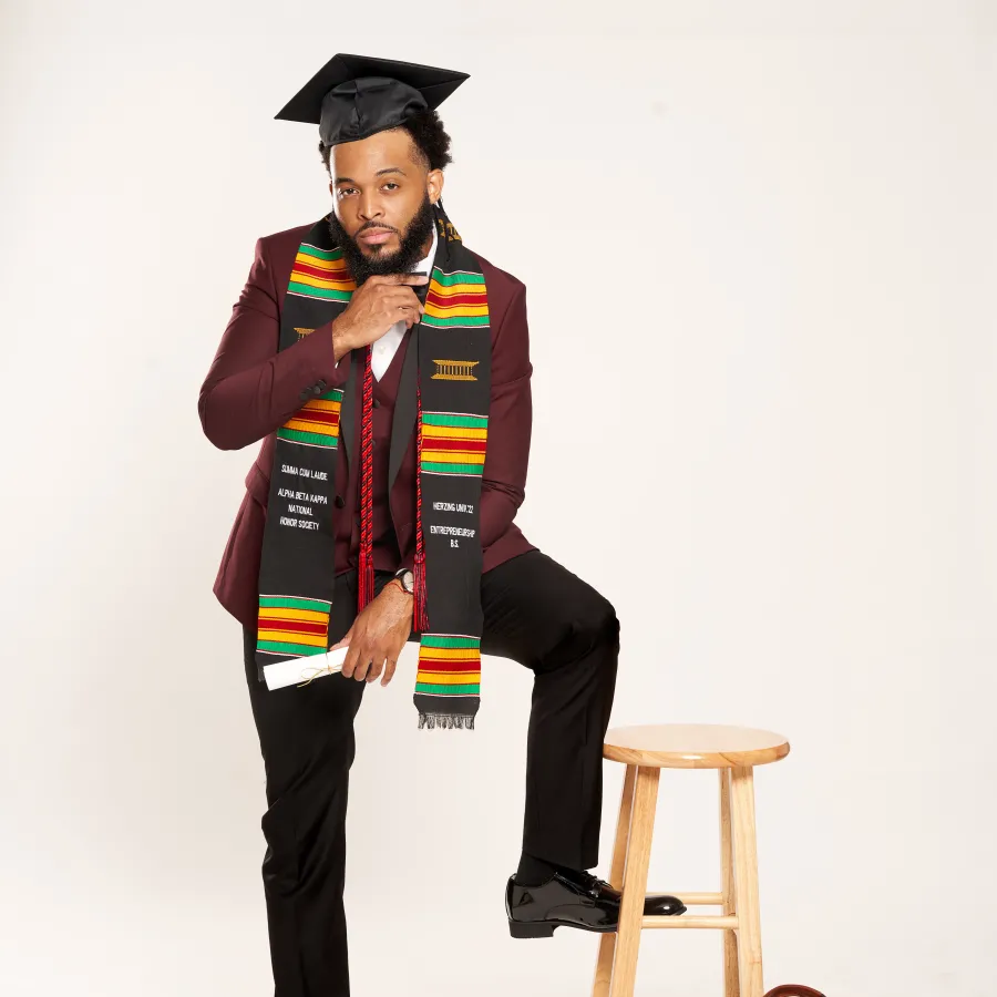 Herzing graduate posing with one foot on a stool in his cap and sash.