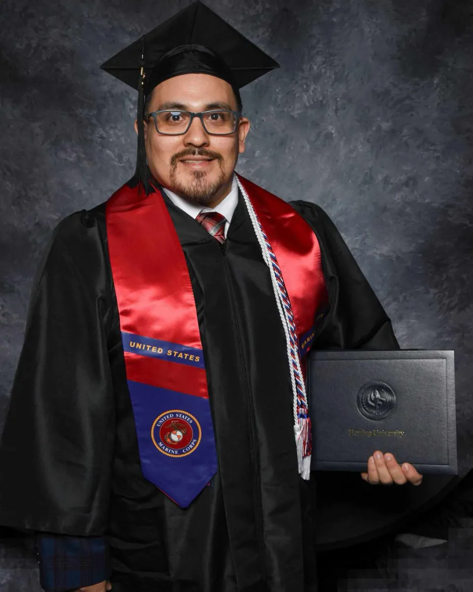 Business management graduate Jon Rodriguez posing in cap and gown holding diploma