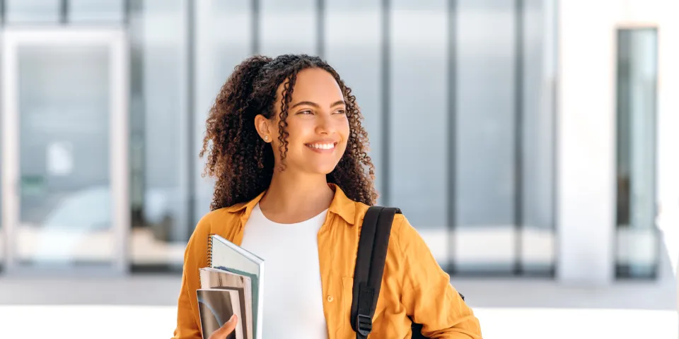 Student wearing backpack and smiling holding textbook