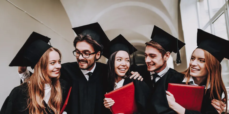 Five college graduates holding diplomas celebrating on graduation day