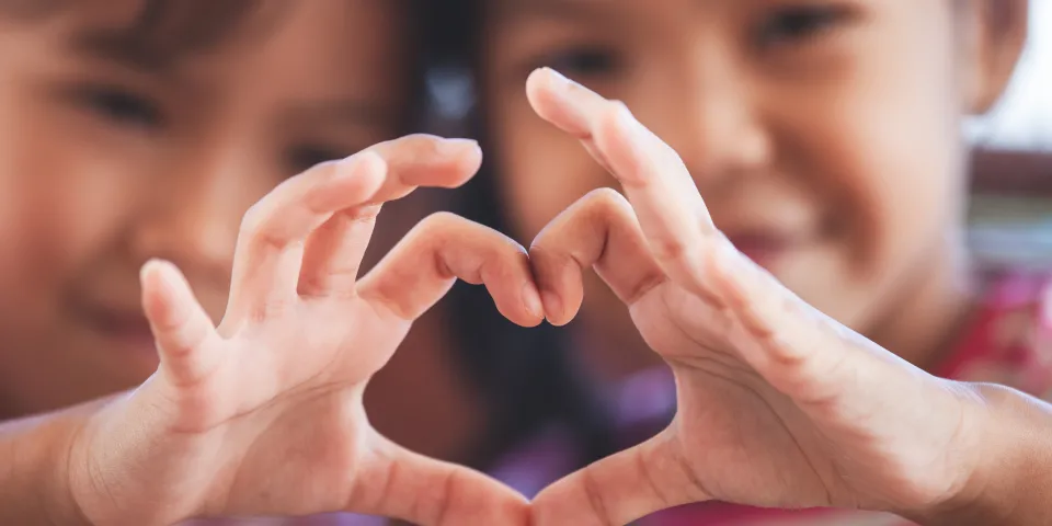 Two cute asian child girls making heart shape with hands together