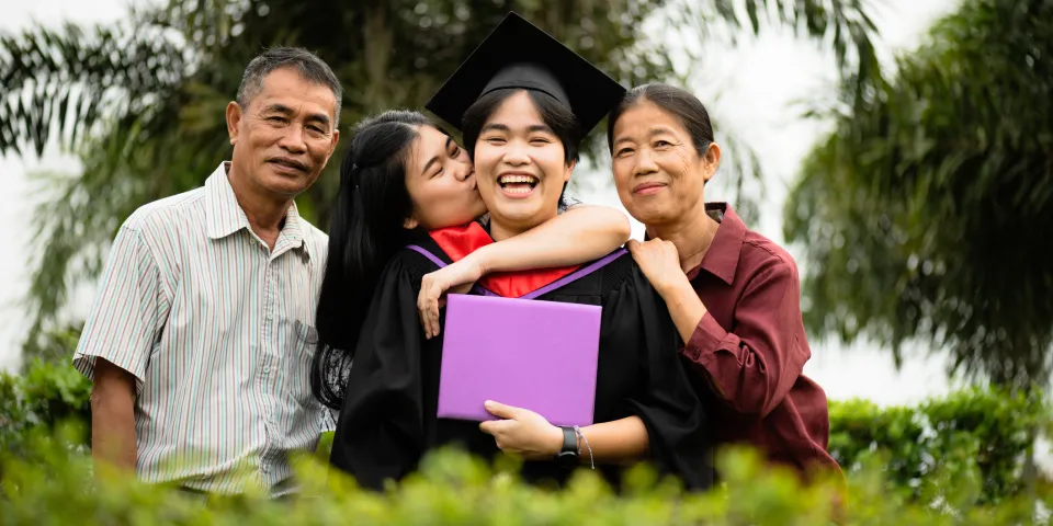 College graduate smiling and holding diploma while celebrating with family