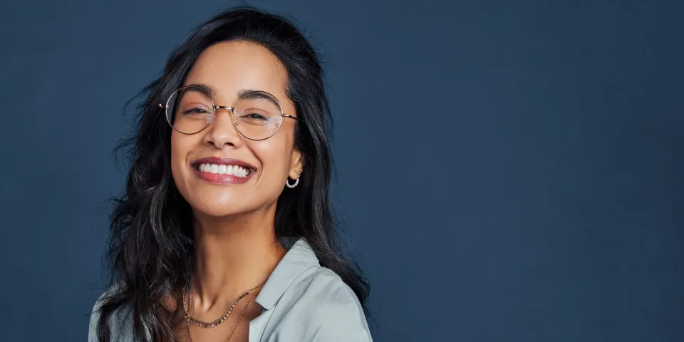 Beautiful university student having fun isolated against blue wall while wearing specs.