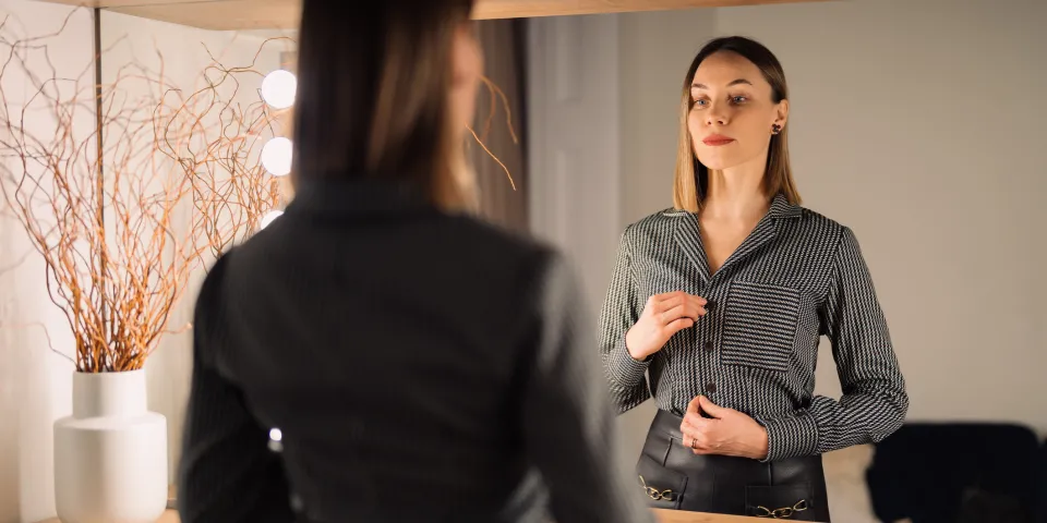 Self-confident woman looking at her reflection into the mirror indoors.