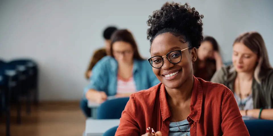 Happy African American woman attending a lecture in university classroom and looking at camera.