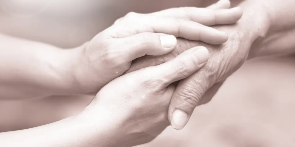 Caregiver, career hand holding elder hand in hospice care. 